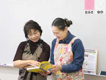 番外編その②　関東「道の駅」スタンプラリー2016を食い入るように見る先生と、アシスタントの斉藤さん。道の駅しもつけでも販売中！