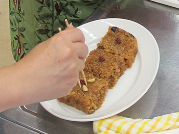 切りわけたらそれぞれに飾り付け♪竹串をお箸のようにして松の実、なつめをお花のように飾っていきましょう。皆さん真剣！飾るものの数は奇数なんですって。